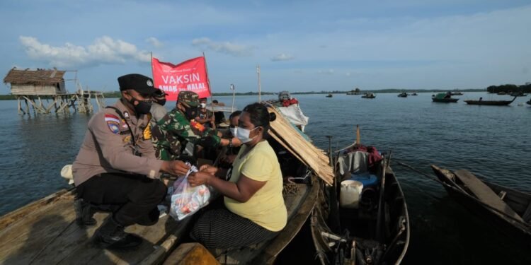 Mengunakan Perahu, Bhabinkamtibmas Desa Berakit Bagikan Masker Dan Sembako Kepada Masyarakat.